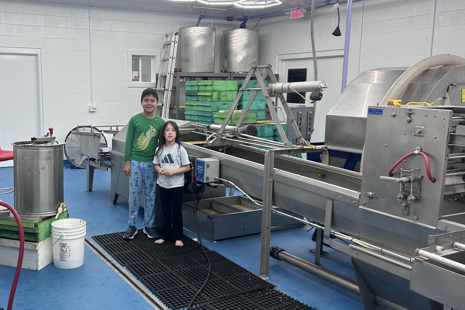 Two of the Lee children in the Lee's Bees honey house, beside the honey-extracting line